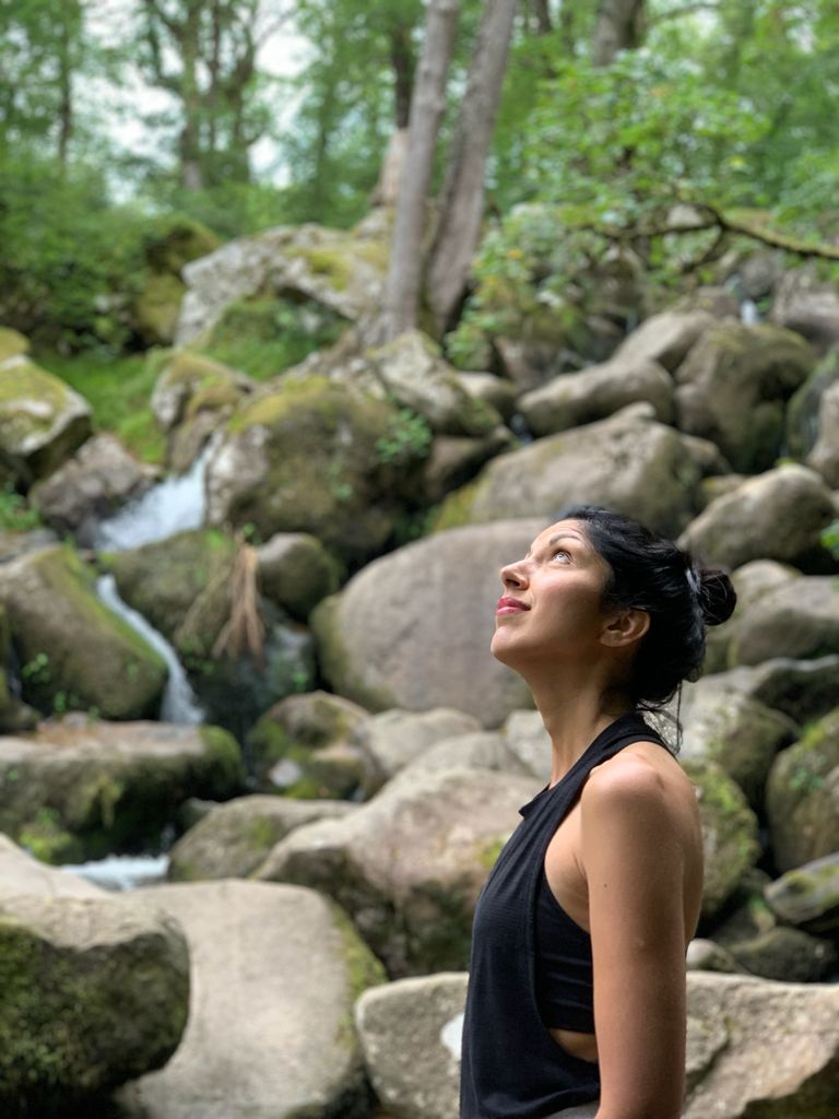 A woman standing looking up to the left with a forest behind her